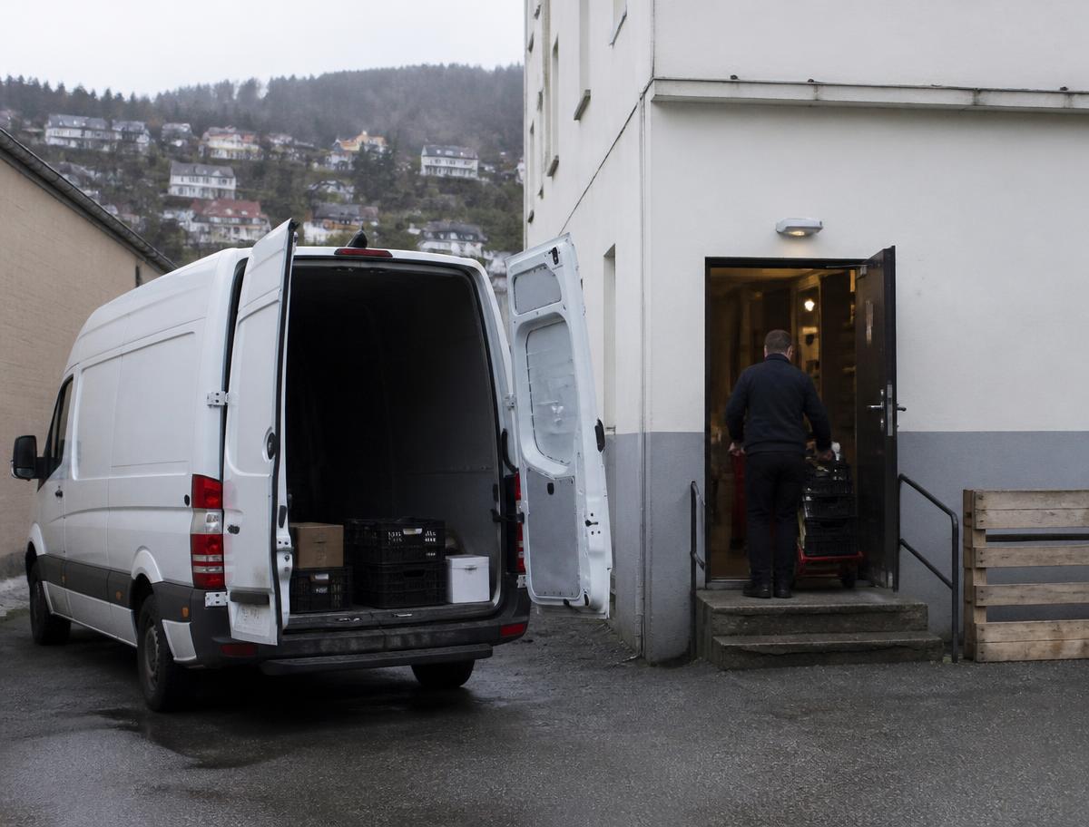 Varebil ved bakinngangen til en butikk der varer trilles inn på sekketralle